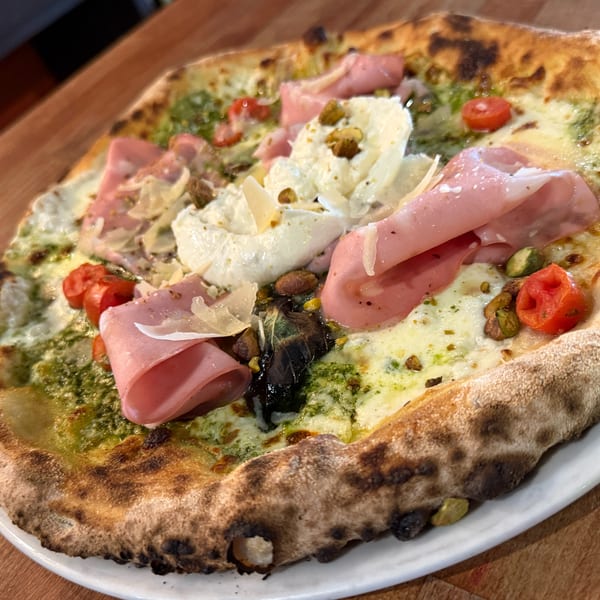 Neapolitan pizza with pesto, mozzarella, prosciutto, cherry tomatoes, and pistachios on a white plate.