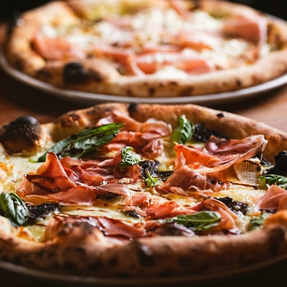 Two delicious pizzas with prosciutto, basil, and cheese on a rustic wooden table.