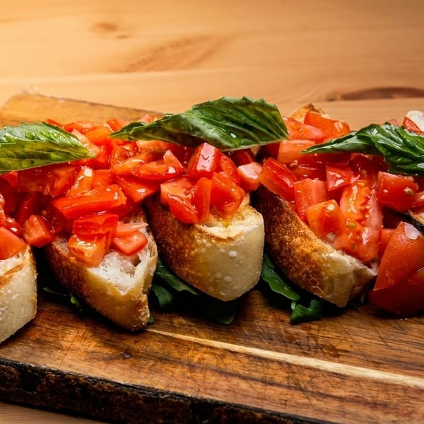 Four bruschetta pieces with diced tomatoes and basil on a wooden board.