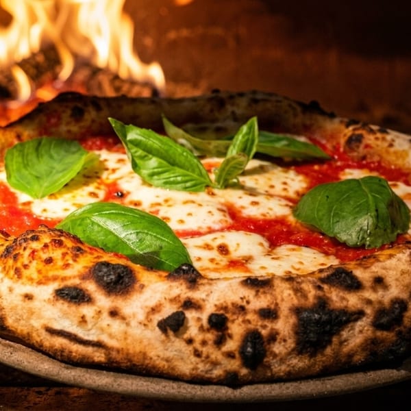 Freshly baked Margherita pizza with basil leaves and melted mozzarella, emerging from a wood-fired oven.