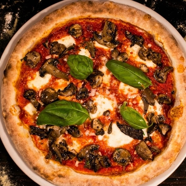 Top-down view of a mushroom and mozzarella pizza with basil leaves on a dark wooden table.