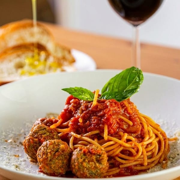 Spaghetti with meatballs and tomato sauce, garnished with basil, served with bread and red wine.
